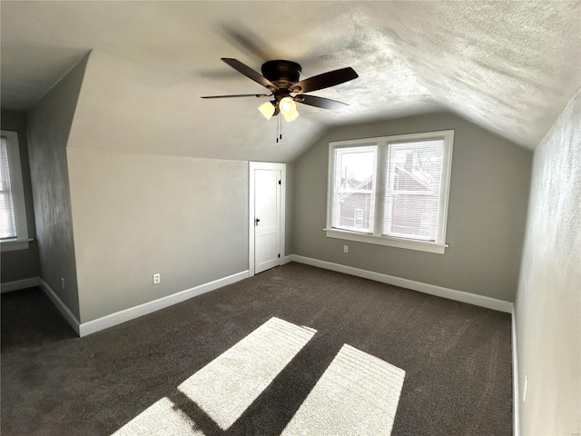 additional living space featuring lofted ceiling, ceiling fan, dark carpet, and a textured ceiling