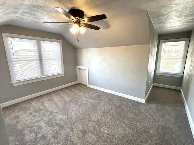 additional living space with dark colored carpet, a textured ceiling, ceiling fan, and vaulted ceiling