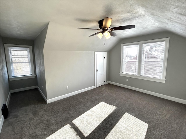 bonus room featuring ceiling fan, a wealth of natural light, lofted ceiling, and dark carpet