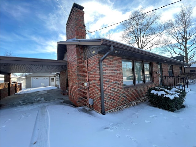 view of snow covered exterior with a garage, an outbuilding, and a carport