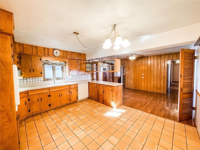 kitchen with sink, dishwasher, hanging light fixtures, wooden walls, and kitchen peninsula