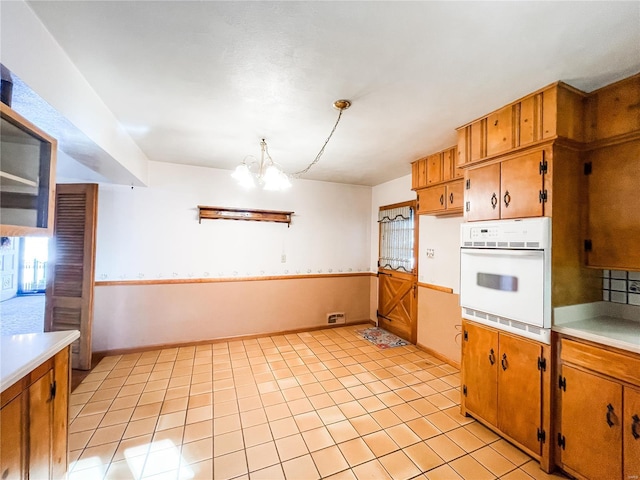 kitchen featuring pendant lighting, oven, a chandelier, and light tile patterned flooring