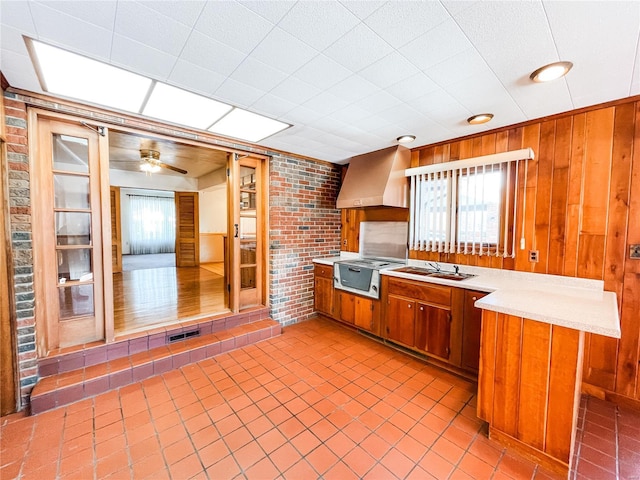 kitchen with sink, wall chimney range hood, wooden walls, and kitchen peninsula