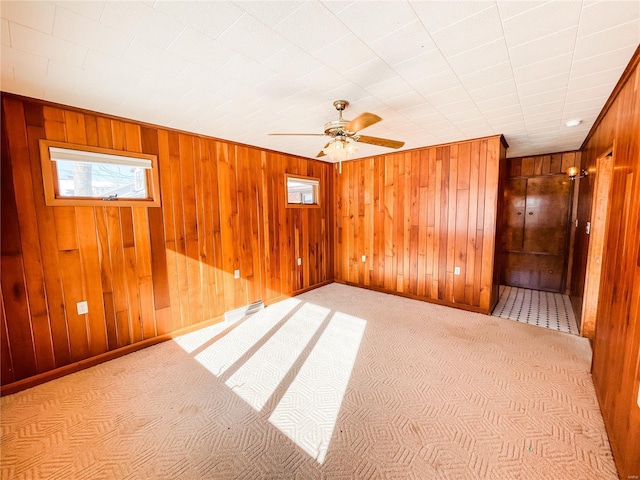 spare room featuring ceiling fan, light carpet, and wooden walls