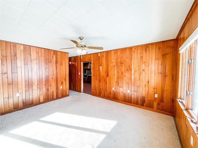 empty room featuring ceiling fan, wooden walls, and light carpet