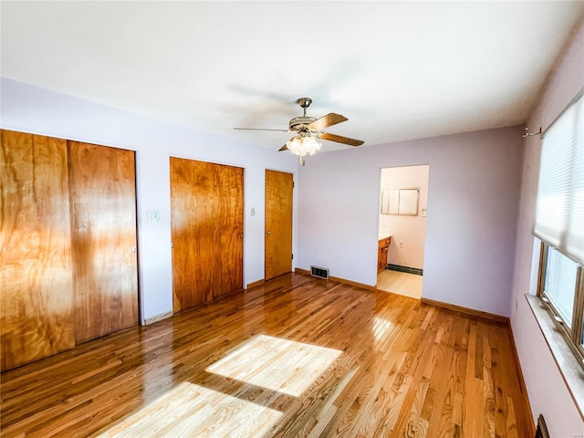 unfurnished bedroom with connected bathroom, two closets, light hardwood / wood-style floors, and ceiling fan