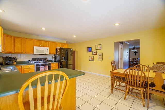 kitchen with gas stove, backsplash, black fridge, ceiling fan, and light tile patterned floors