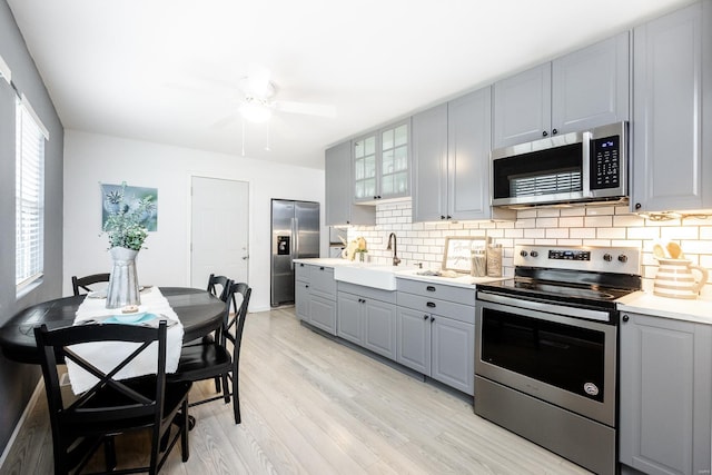 kitchen featuring sink, gray cabinets, stainless steel appliances, light hardwood / wood-style floors, and backsplash