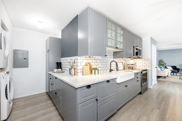 kitchen with appliances with stainless steel finishes, sink, gray cabinetry, stacked washer / drying machine, and electric panel