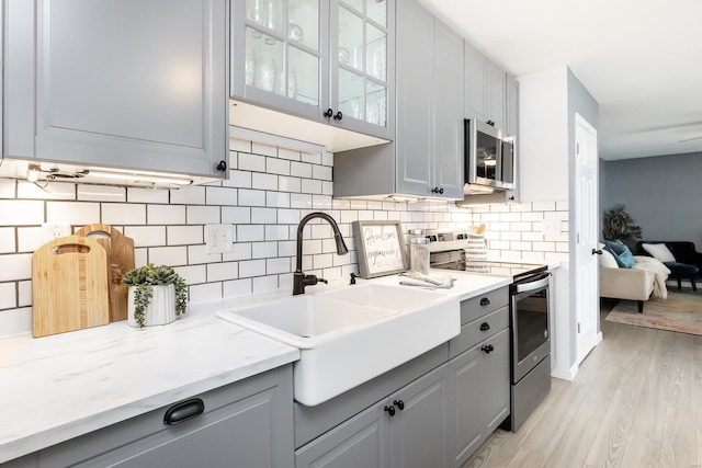 kitchen featuring tasteful backsplash, sink, gray cabinetry, stainless steel appliances, and light wood-type flooring