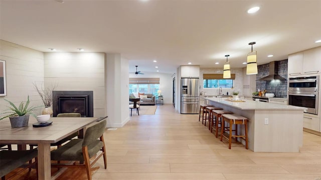 kitchen with wall chimney exhaust hood, white cabinetry, decorative light fixtures, appliances with stainless steel finishes, and a kitchen island