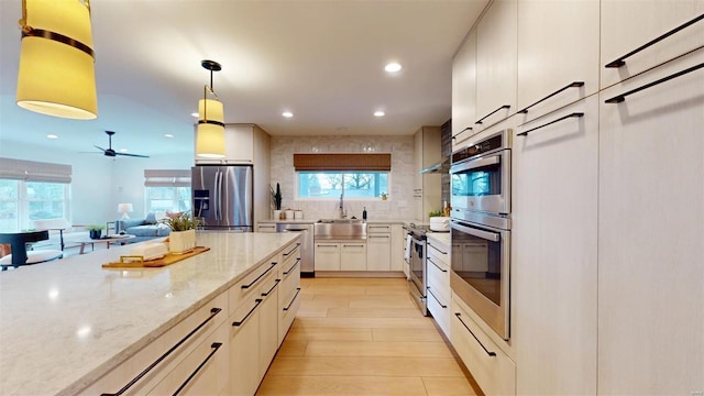 kitchen with sink, hanging light fixtures, stainless steel appliances, light stone counters, and a wealth of natural light