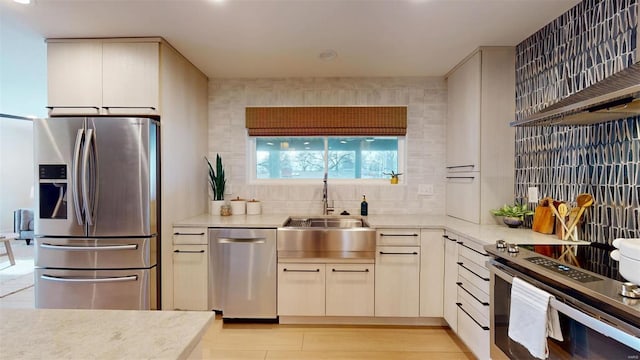 kitchen featuring sink, appliances with stainless steel finishes, light hardwood / wood-style floors, decorative backsplash, and wall chimney exhaust hood