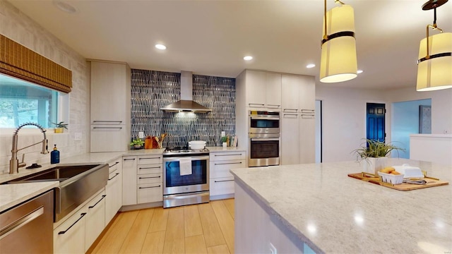 kitchen featuring white cabinetry, stainless steel appliances, hanging light fixtures, and wall chimney range hood