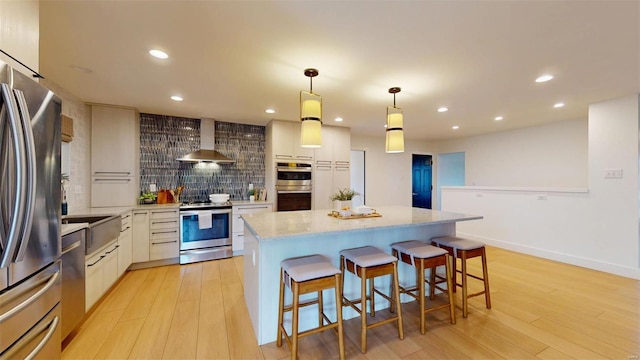 kitchen featuring light hardwood / wood-style flooring, hanging light fixtures, wall chimney range hood, stainless steel appliances, and white cabinets