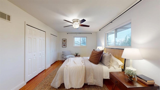 bedroom with multiple closets, wood-type flooring, and ceiling fan