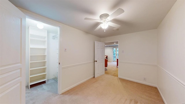 unfurnished bedroom featuring light carpet, a walk in closet, a closet, and ceiling fan