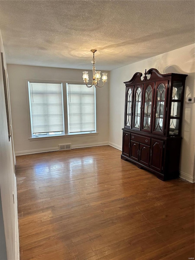 unfurnished dining area featuring a notable chandelier, a textured ceiling, and hardwood / wood-style flooring