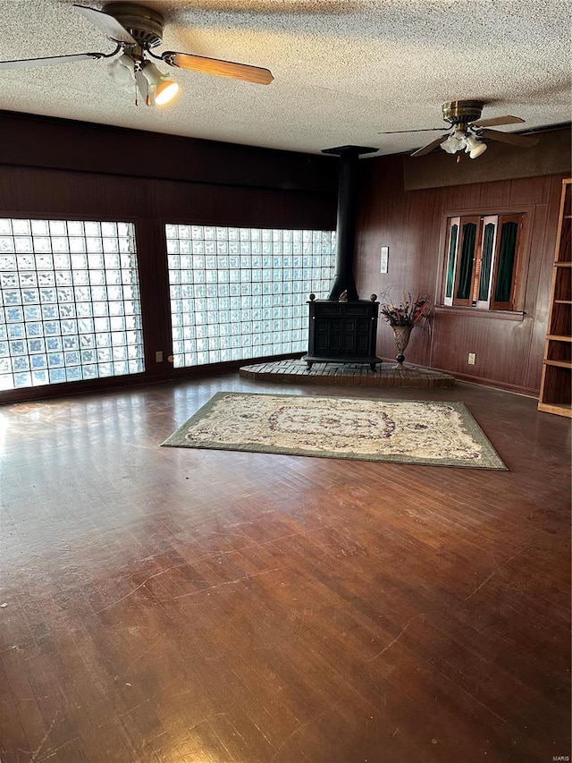 unfurnished living room with a textured ceiling, dark hardwood / wood-style flooring, a wood stove, and wooden walls