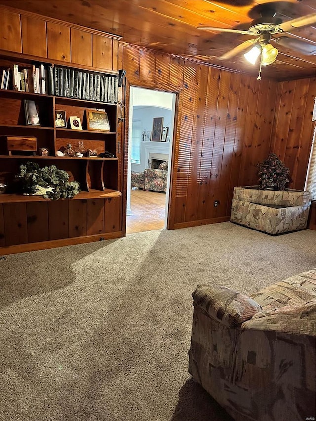 living area with carpet floors, wooden ceiling, wood walls, and ceiling fan