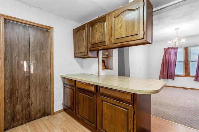 kitchen featuring hanging light fixtures, brick wall, kitchen peninsula, light hardwood / wood-style flooring, and an inviting chandelier