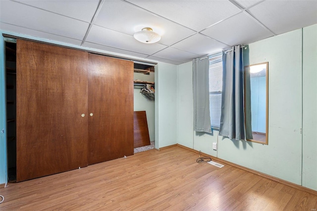 unfurnished bedroom with a drop ceiling, a closet, and light wood-type flooring