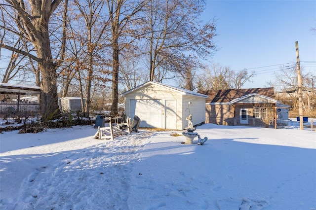 snowy yard with a garage and an outbuilding