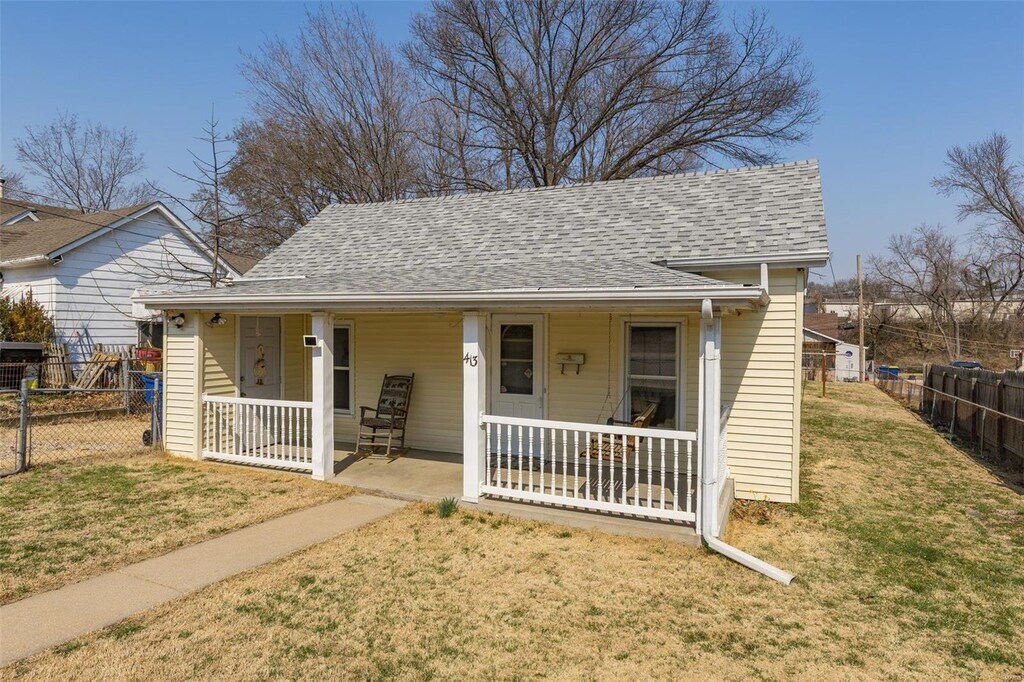 bungalow-style house featuring a front yard, fence, covered porch, and a shingled roof