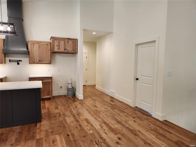 kitchen with a towering ceiling, decorative light fixtures, and light hardwood / wood-style flooring