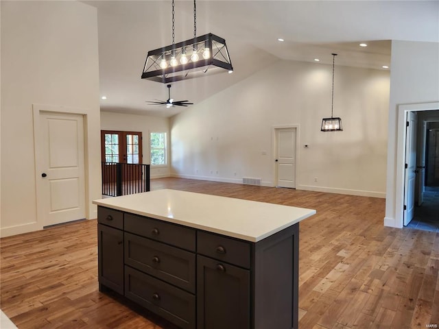 kitchen with light hardwood / wood-style flooring, a center island, decorative light fixtures, high vaulted ceiling, and ceiling fan