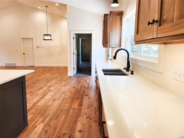 kitchen featuring sink, high vaulted ceiling, light hardwood / wood-style flooring, and hanging light fixtures