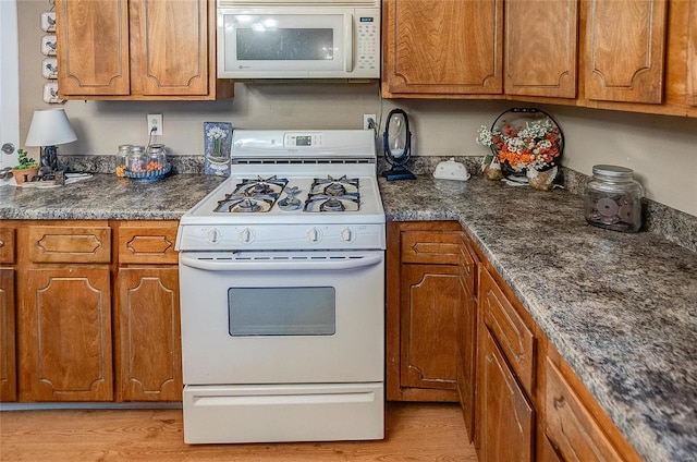 kitchen with light hardwood / wood-style floors, white appliances, and dark stone countertops