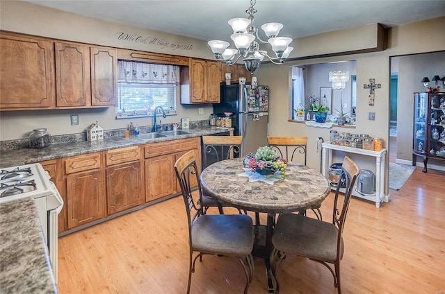 kitchen with pendant lighting, sink, stainless steel fridge, a notable chandelier, and light wood-type flooring