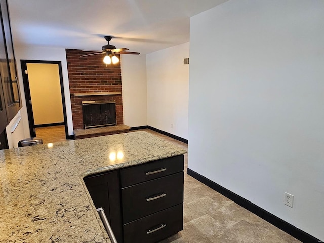 kitchen featuring a brick fireplace, ceiling fan, and light stone counters