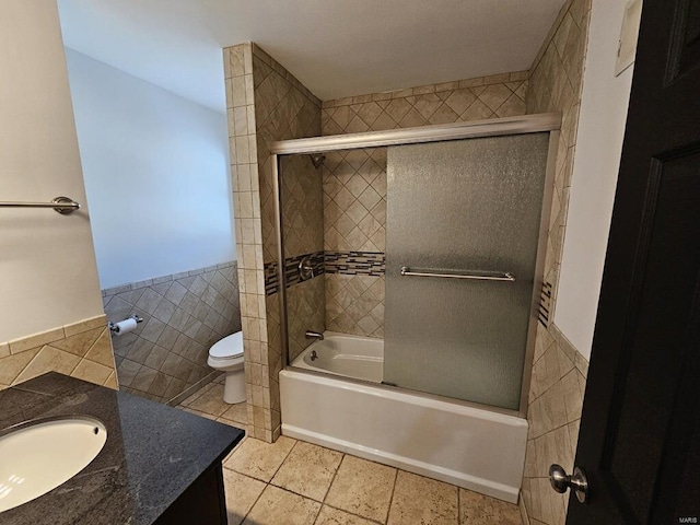 full bathroom featuring tile patterned flooring, toilet, combined bath / shower with glass door, vanity, and tile walls