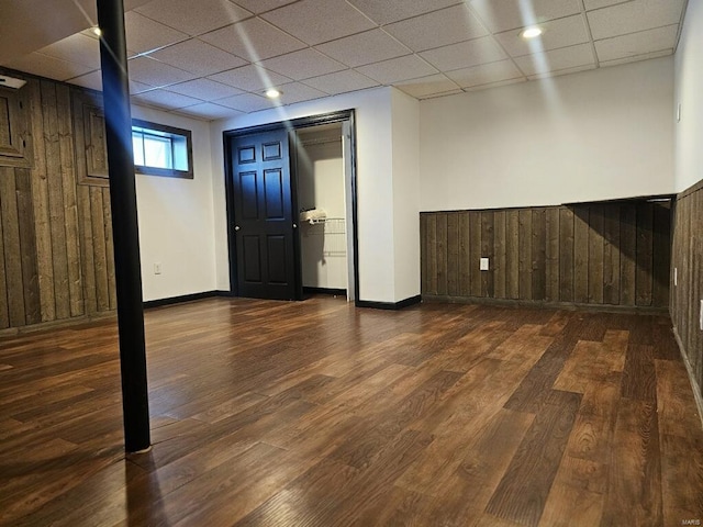 basement featuring a paneled ceiling, wood walls, and dark hardwood / wood-style floors