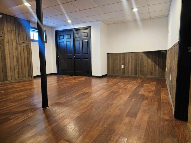 basement featuring wood walls, a drop ceiling, and dark hardwood / wood-style floors