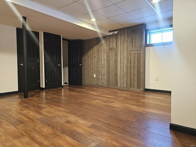 basement featuring wooden walls, hardwood / wood-style flooring, and a drop ceiling