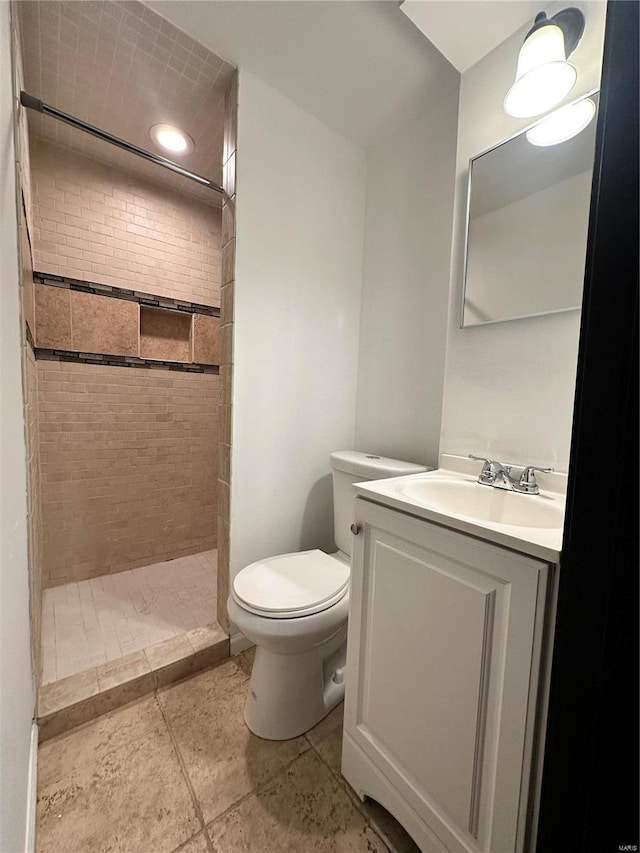 bathroom featuring toilet, a tile shower, and vanity