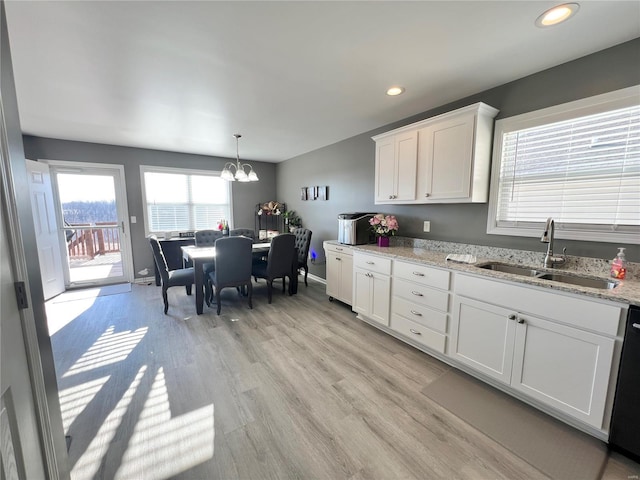 kitchen featuring light stone countertops, dishwashing machine, white cabinetry, an inviting chandelier, and sink