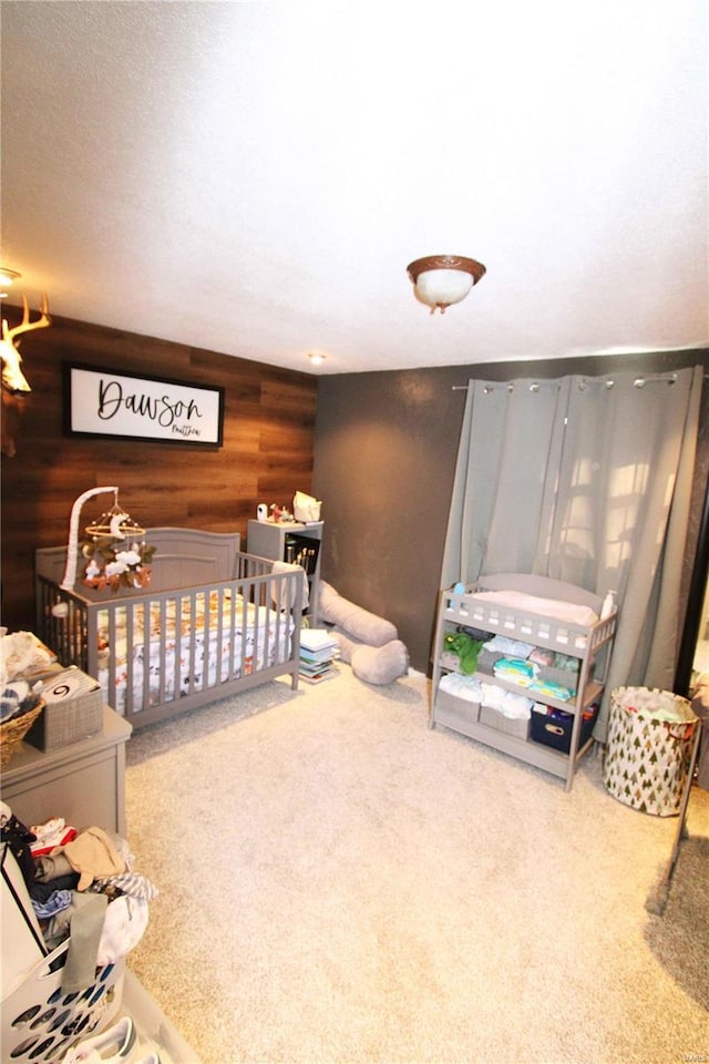 bedroom with a crib, wood walls, and carpet