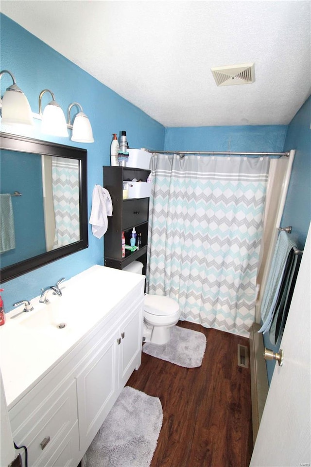 bathroom with a textured ceiling, toilet, vanity, and wood-type flooring