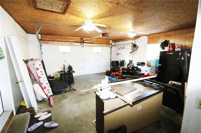 garage with ceiling fan, black fridge, wooden walls, and a garage door opener