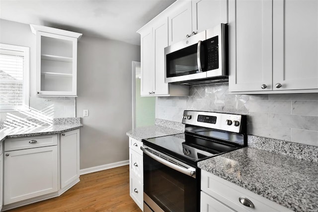 kitchen with light wood-type flooring, appliances with stainless steel finishes, white cabinetry, and light stone countertops