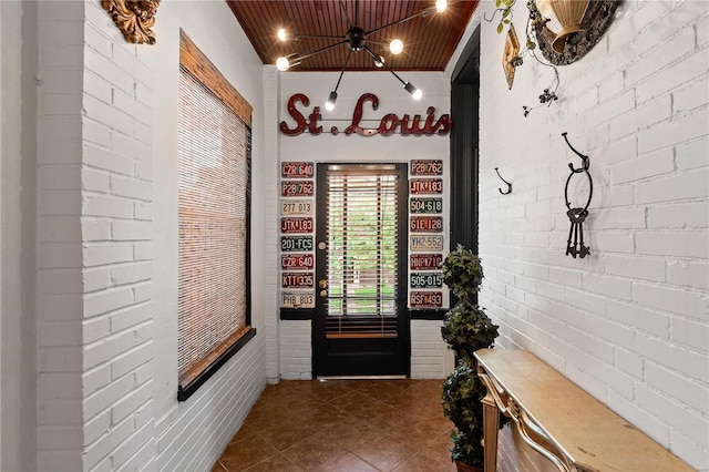 interior space with brick wall, dark tile patterned floors, and wood ceiling