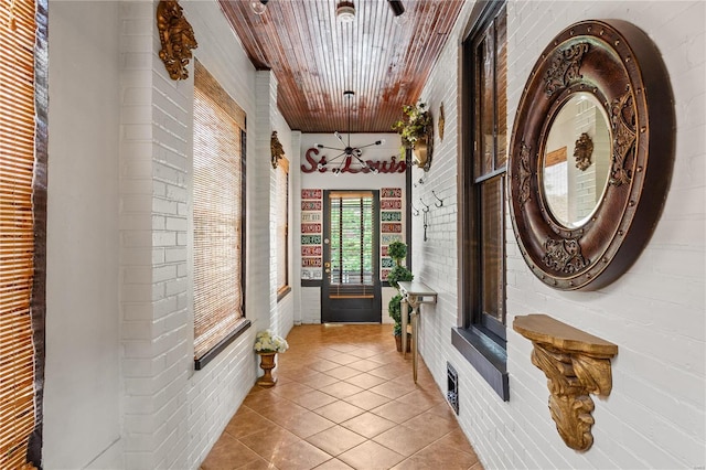 hallway with light tile patterned floors, wood ceiling, and brick wall