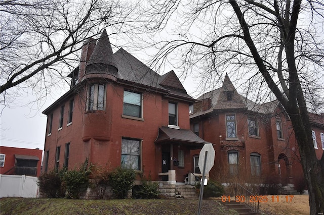 victorian house featuring brick siding, a chimney, and fence