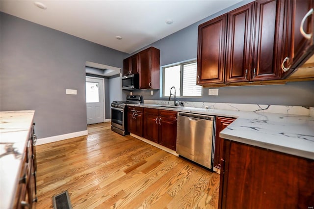 kitchen with sink, stainless steel appliances, light stone counters, and light hardwood / wood-style floors