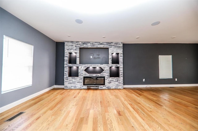 unfurnished living room with hardwood / wood-style flooring and a stone fireplace