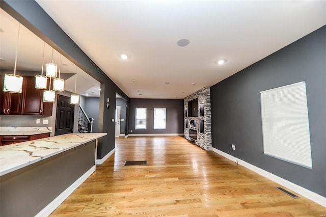 kitchen with light hardwood / wood-style flooring, hanging light fixtures, a stone fireplace, light stone counters, and dark brown cabinetry